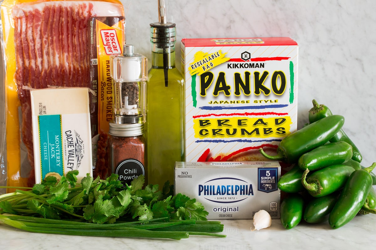 Photo of ingredients used to make jalapeno poppers. Includes fresh jalapenos, panko bread crumbs, cream cheese, garlic, cilantro, green onions, Monterey jack cheese, chili powder, salt, pepper and bacon. 